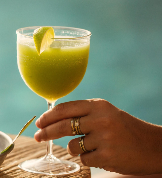 a green drink in a tall glass being held by a gentle hand