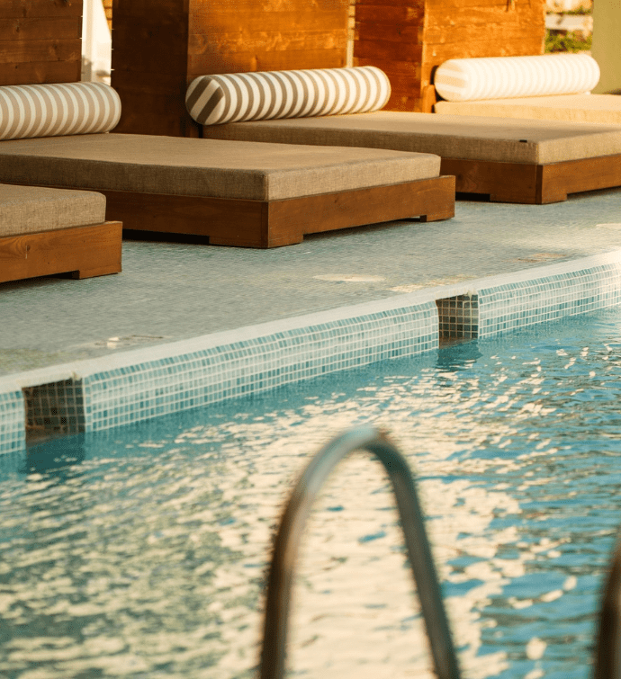 a calm scene with a glimpse of the pool with luxurious lounge chairs