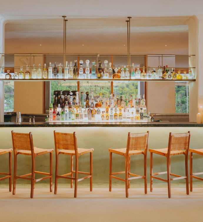 Modern bar with light wooden barstools, light green blacksplash, and rows of bottles of liquor