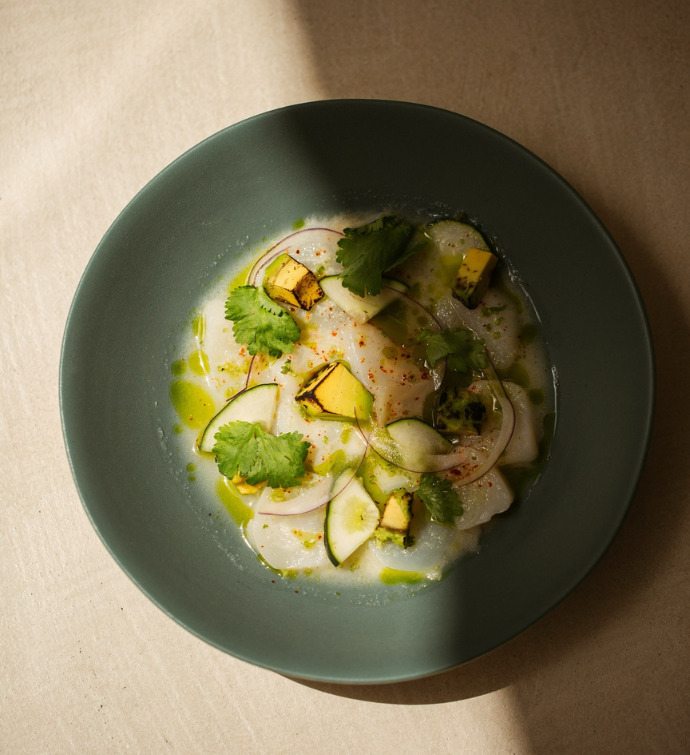 Seafood dish with green garnish on a blue plate on a beige surface