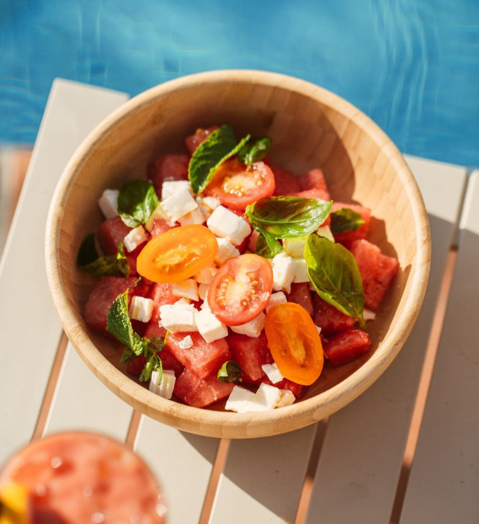 Bowl of tomato salad sitting on a beige table with a pool in the background