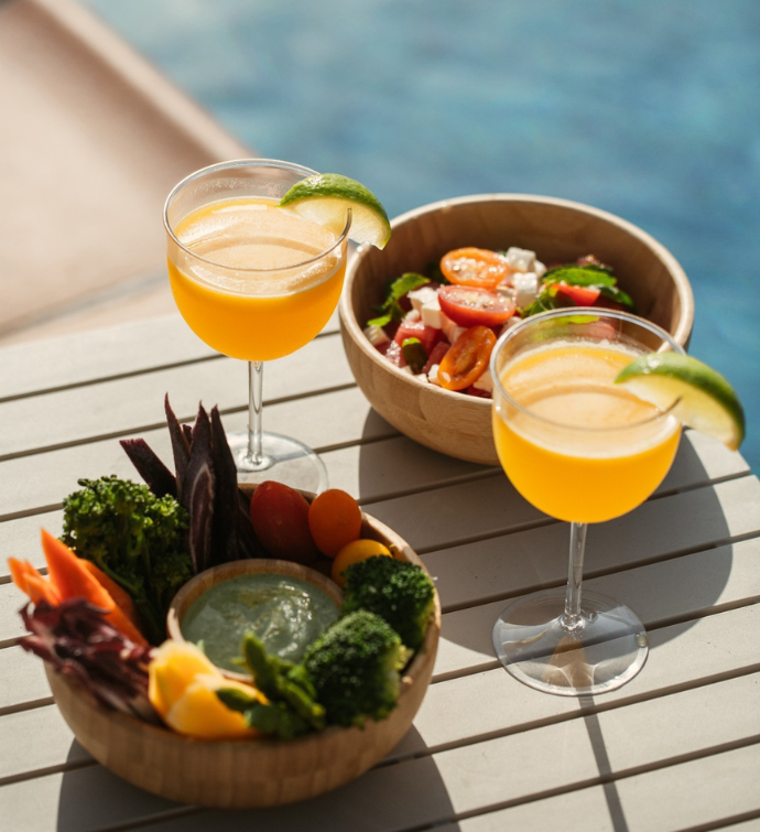 two yellow cocktails garnished with lemon on a side table with clear blue water in the background