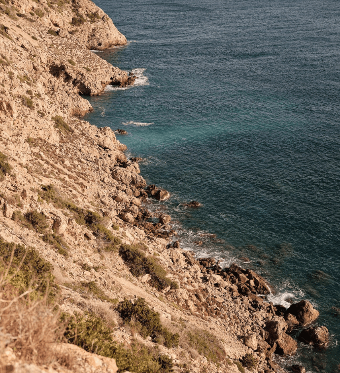 a rocky beach hillside that leads to dark blue waters
