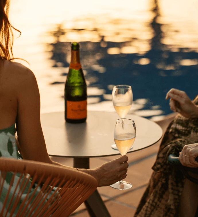 two people sitting at a table with a bottle of white wine looking at the pool during golden hour