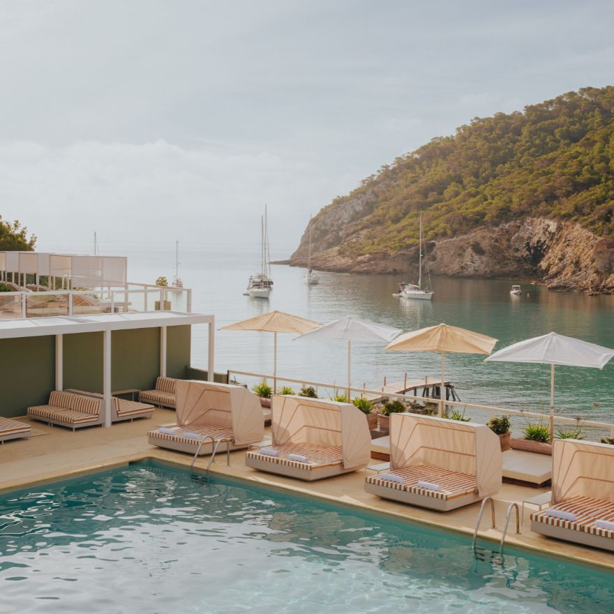 Pool with cabana lounges and striped umbrellas with an ocean and mountains in the background