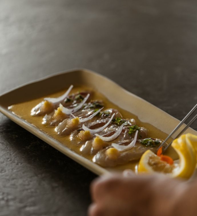 Sashimi on a light yellow rectangular plate with chopsticks and a hand in the background