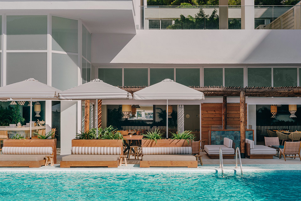 Turquoise pool with three chaise lounges and striped umbrellas over them with building in the back