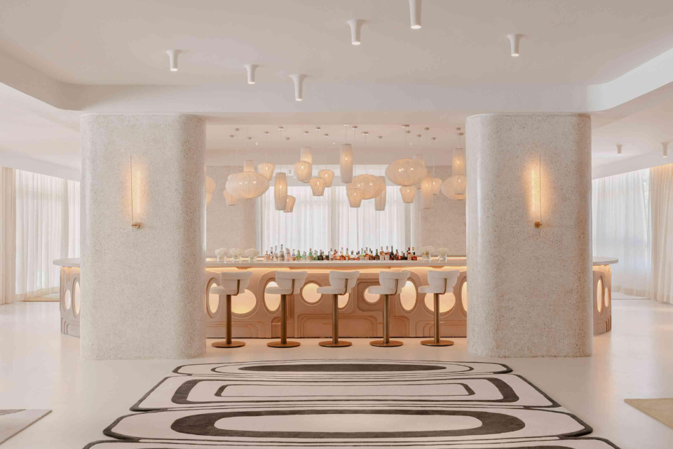 Beautiful modern white bar with white pendant lights, black and white geometric rug, and barstools.