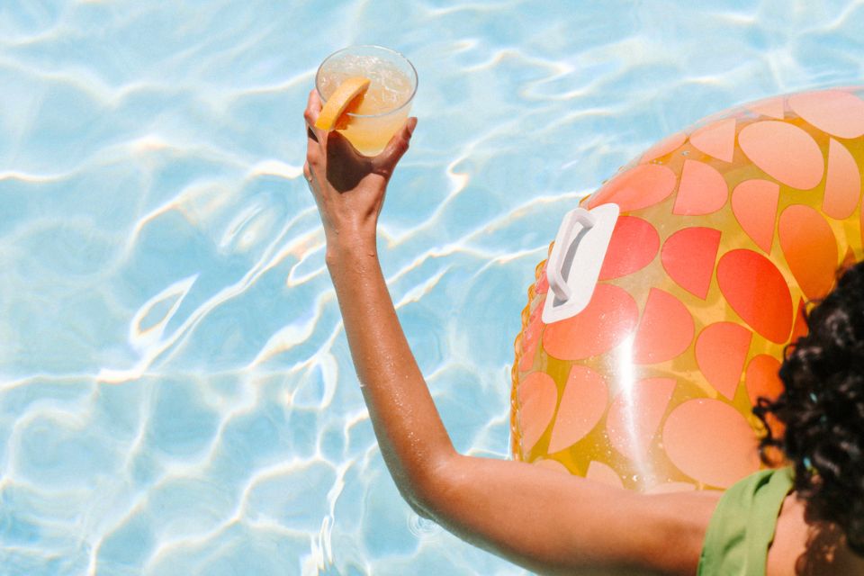 Woman in a pool float holding a cocktail over the pool