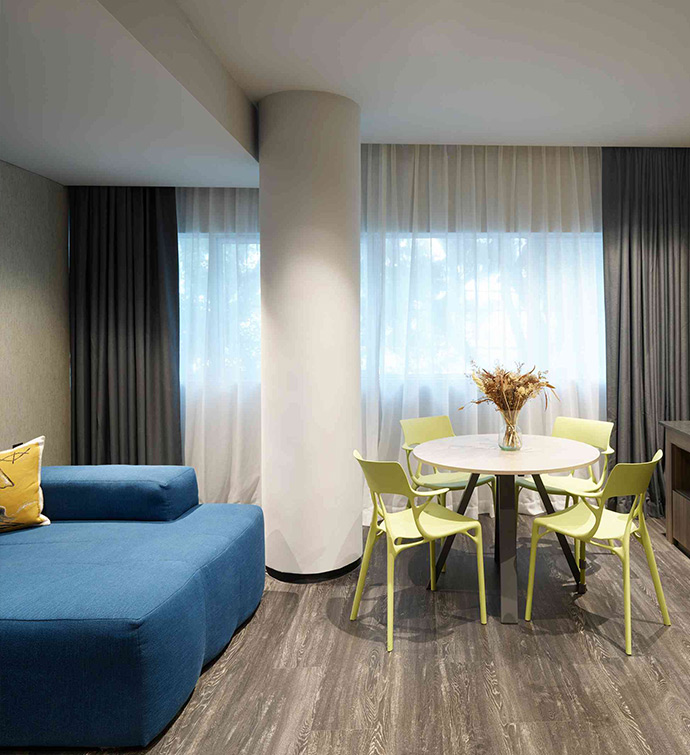 A contemporary hotel room featuring a blue couch, yellow chairs, and a table.