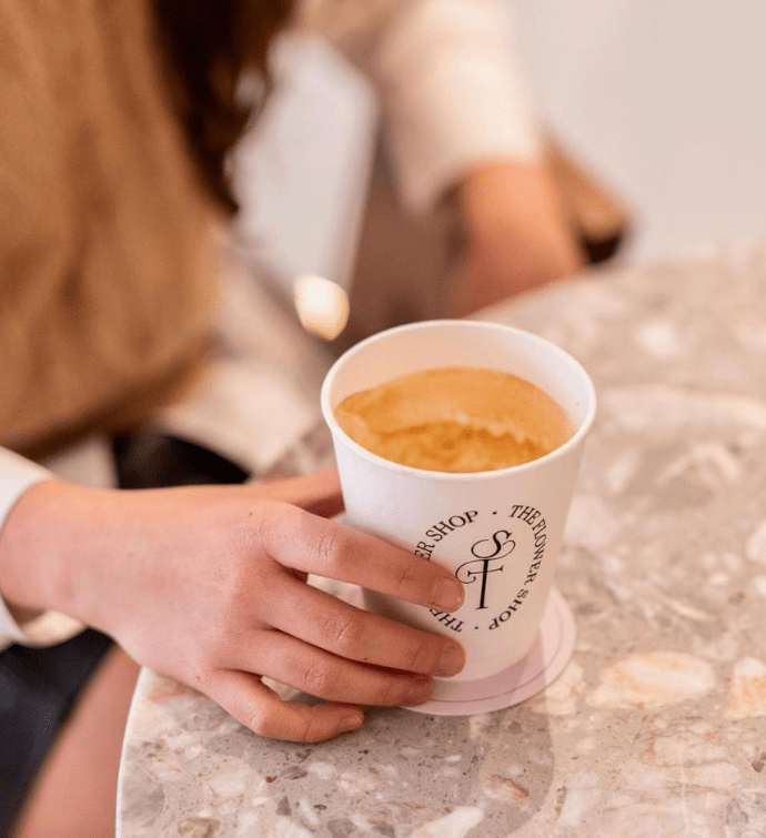 a hand on a table holding a latte in a to-go cup 