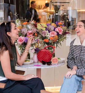 Two women at a small round table with flower bouquet on top of it