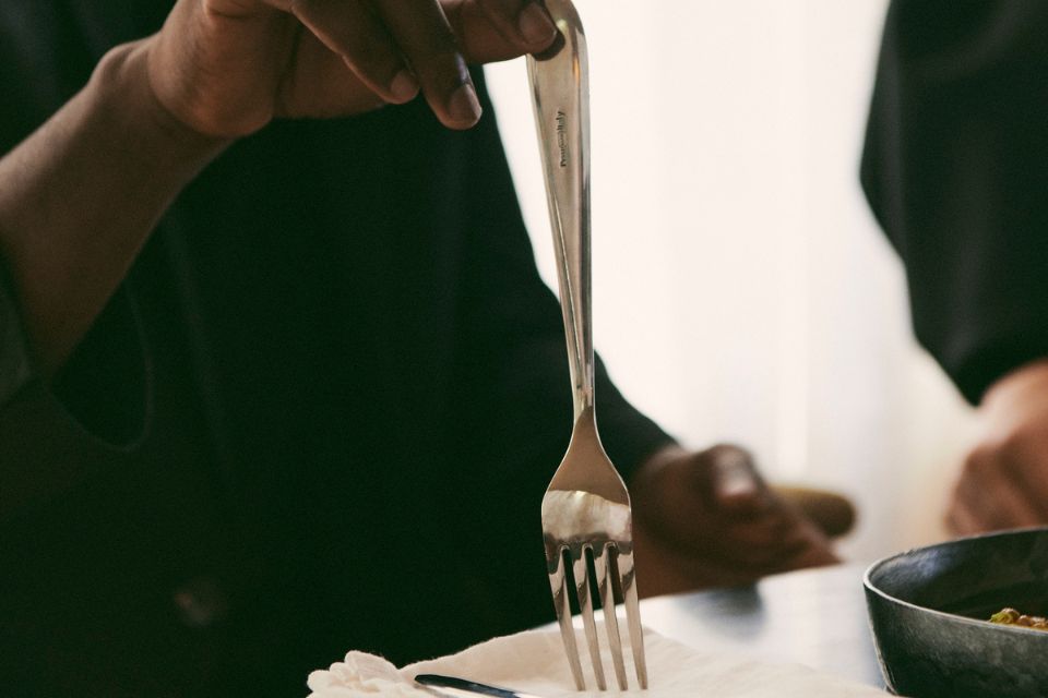 Close up of a fork and a person's hand holding it with their torso in a black shirt in the background