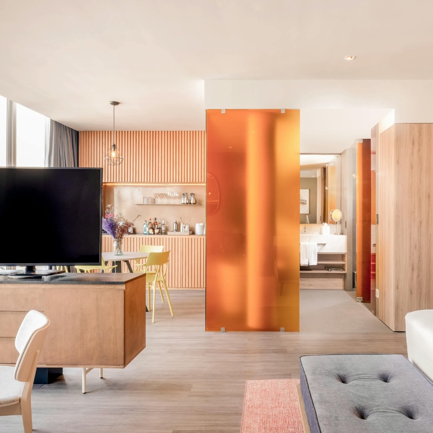 an image of a room with natural light a large king bed and an orange glass divider