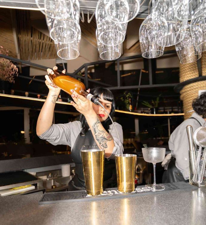 Female bartender pours a drink into a gold shaker