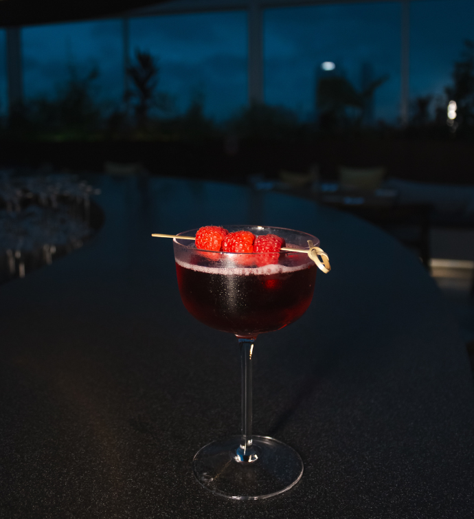 a cocktail sitting on the bar garnished with three raspberries