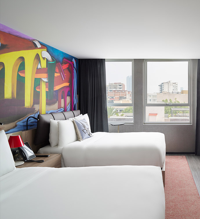 Hotel room with two beds and vibrant mural featuring abstract shapes and colors.