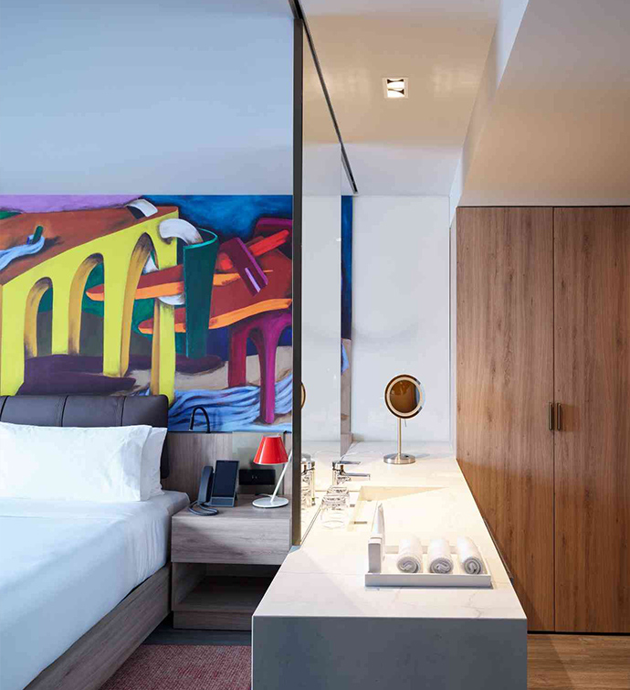 A hotel room with a bed, bathroom, and vibrant mural on the wall.