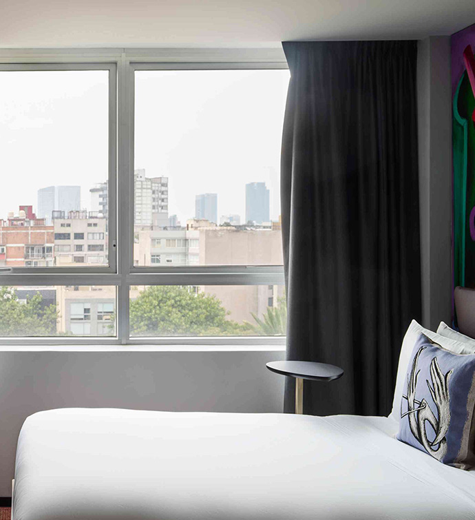 A cozy bed with a white comforter next to a window.