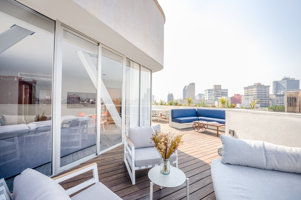 Large terrace with white and light grey sofa and chairs and a small white round table with plant on top and city in the skyline.