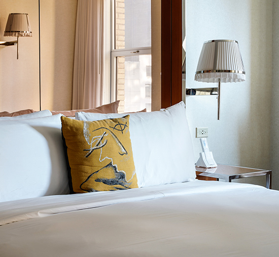 A bed with a yellow pillow on it and a lamp on the wall.