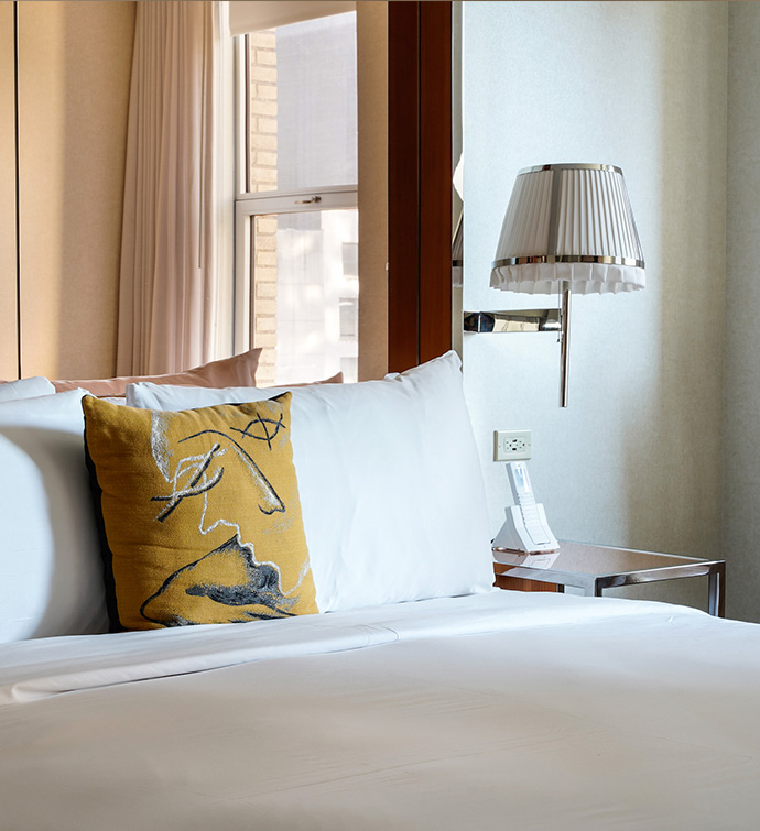 A bed with a yellow pillow on it and a lamp on the wall.