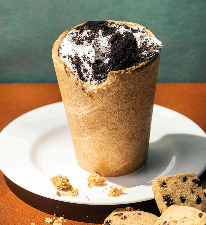 Oreo ice cream in a cookie crust cup sitting on a round white dish with cookies off to the side.