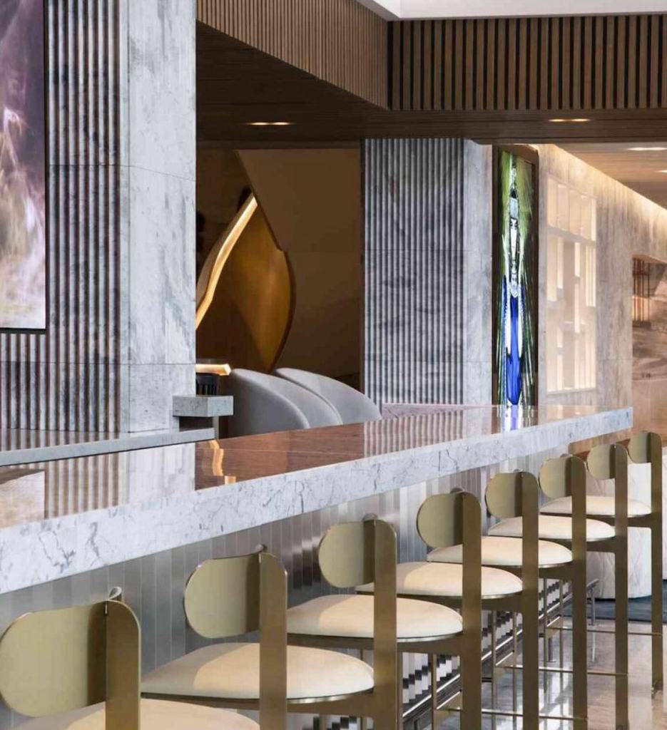 Angled view of a marbled bar with gold barstools lined up against it.