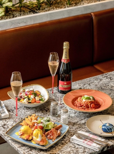 Food on different size and colored plates on grey marble tabletop with a bottle of champagne and two champagne glasses