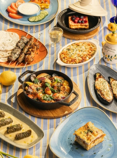 Multiple Mediterranean dishes on different size and color plates on a blue and yellow striped tablecloth