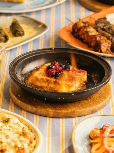 Close up shot of saganaki in a black bowl on a blue and yellow striped tablecloth