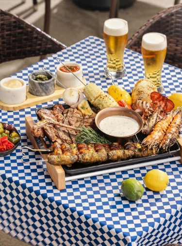 Surf and turf platter with two glasses of beer on a blue and white checkered tablecloth