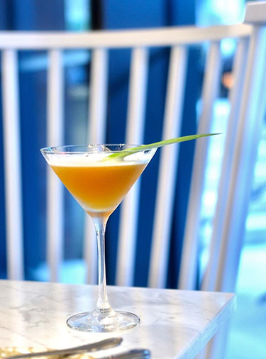 Orange cocktail in a martini glass sitting on a table in front of a white chair