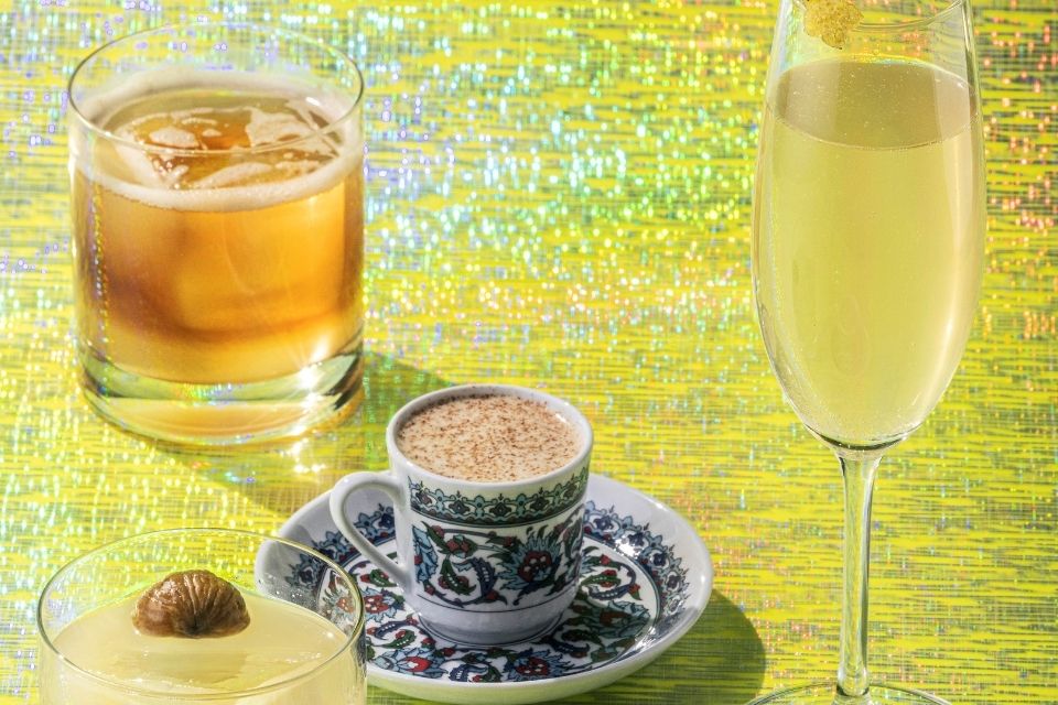 Three cocktails in various sized glasses with a coffee cup on a small saucer plate all on a sparkly yellow background