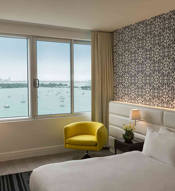 Hotel room with bed, yellow chair, and window overlooking the water.