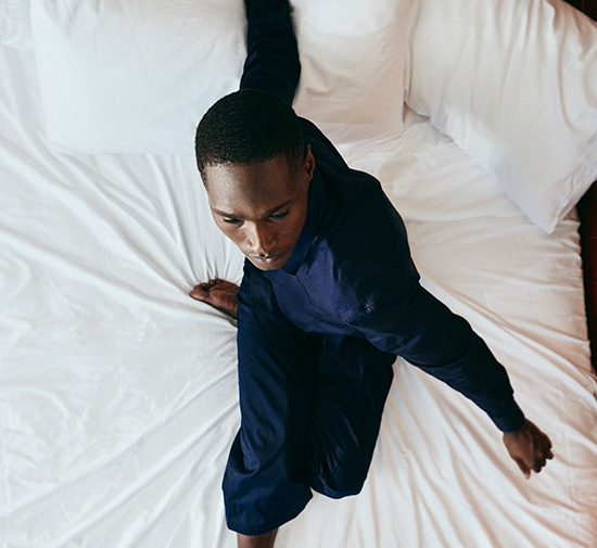 A man sitting on a bed, looking relaxed and comfortable.