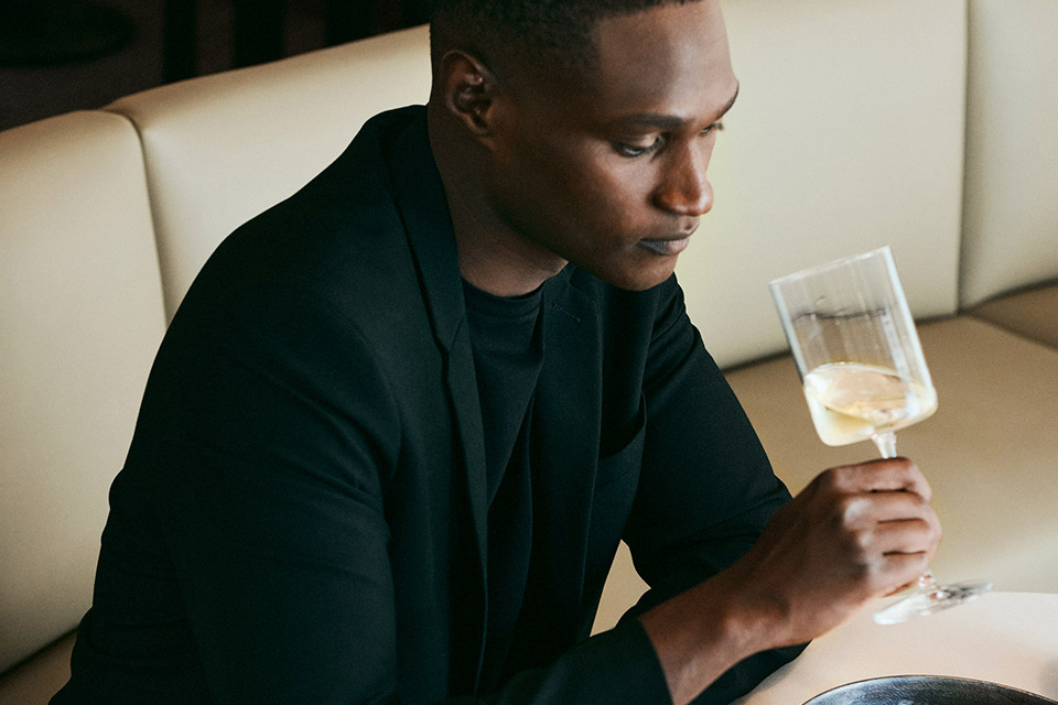 Man in a black suit drinking a glass of white wine