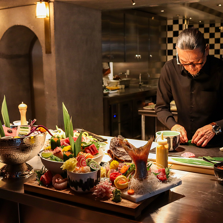 Chef Morimoto cooking on a table with several prepared dishes in the foreground