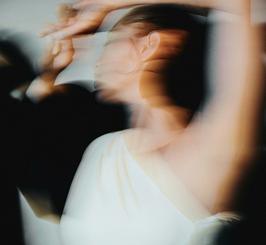 Blurry image depicting a woman in a white one shoulder dress dancing in motion.