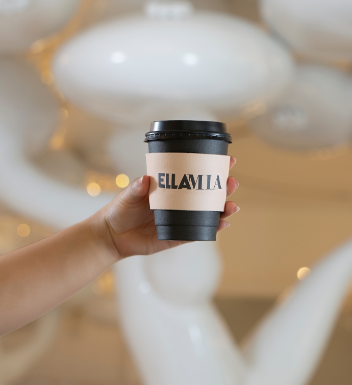 Hand holding a black coffee cup with an EllaMia coffee sleeve