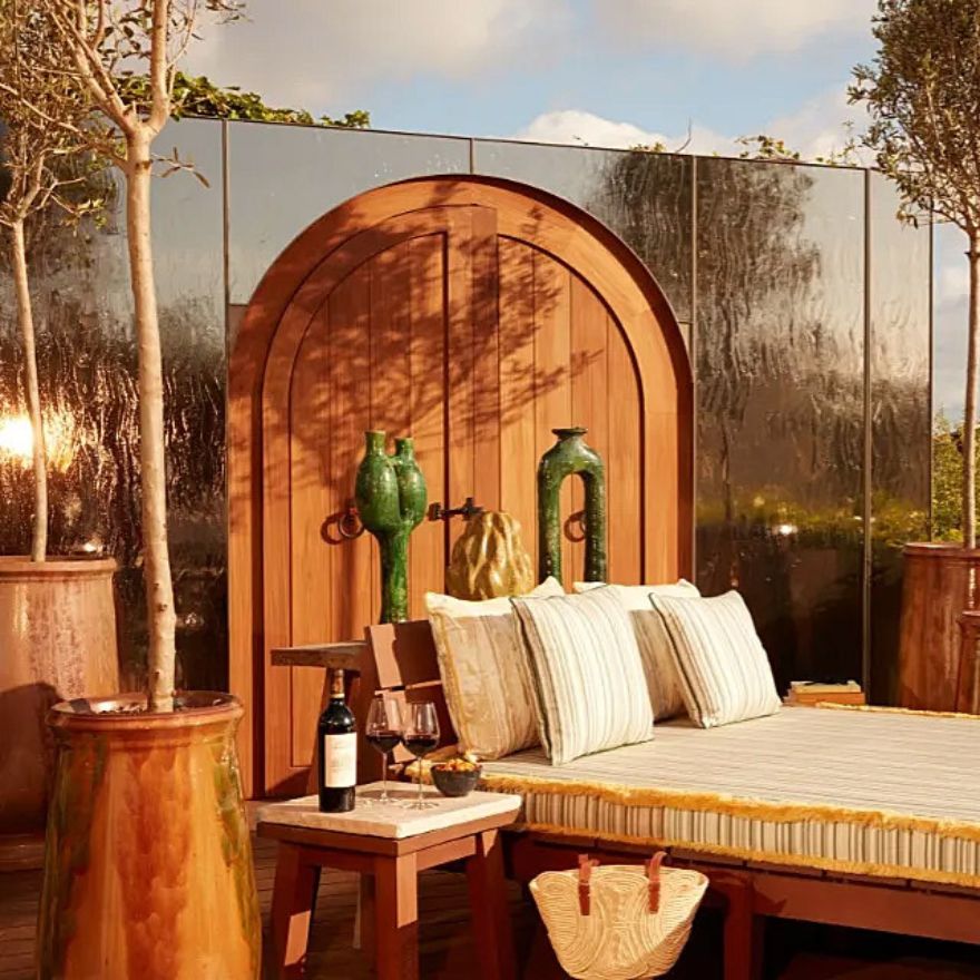 A daybed on a patio accompanied by a table, trees and a purse.