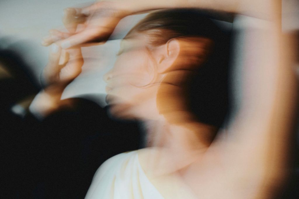 Blurry image depicting a woman in a white one shoulder dress dancing in motion.