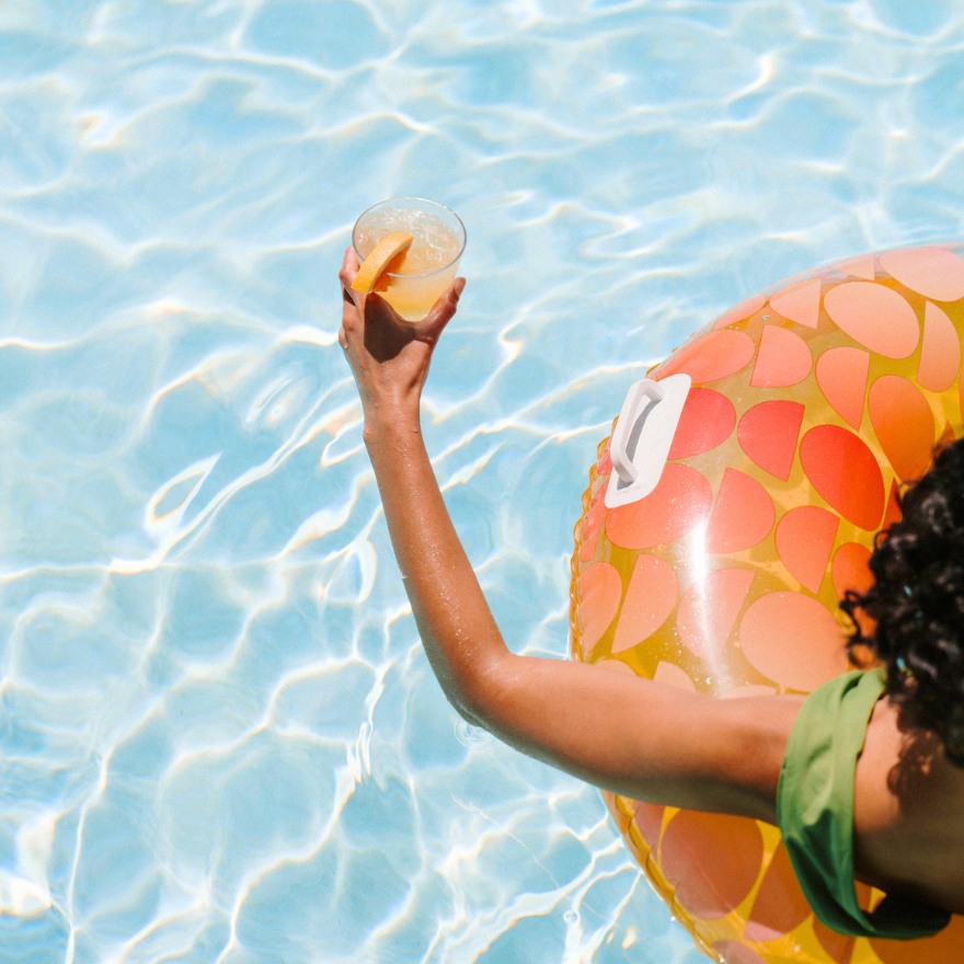 Woman in a pool float holding a cocktail over the pool