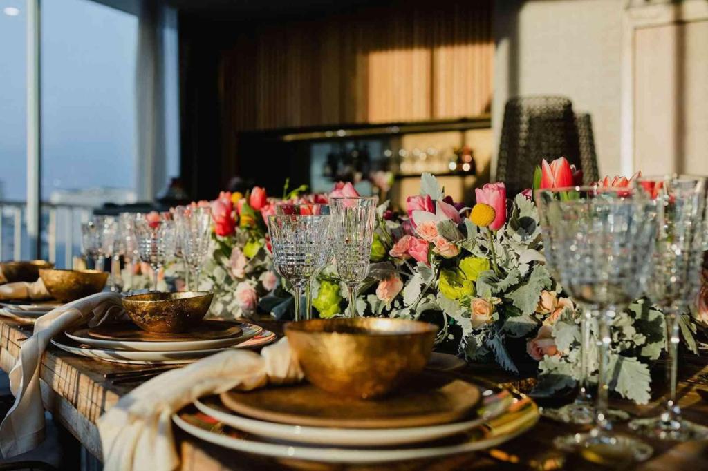 a beautiful table set with gold plates and bowls, crystal champagne and wine glasses and pink tulips.