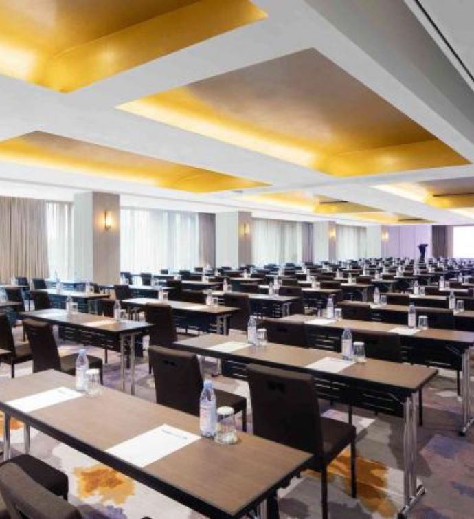 Large meeting room space with rows of desks and chairs with water bottles and paper on top of each desk