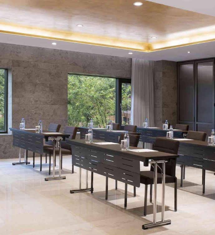 Modern meeting room with a few rows of dark tables and chairs with water bottles and notepads on the tables