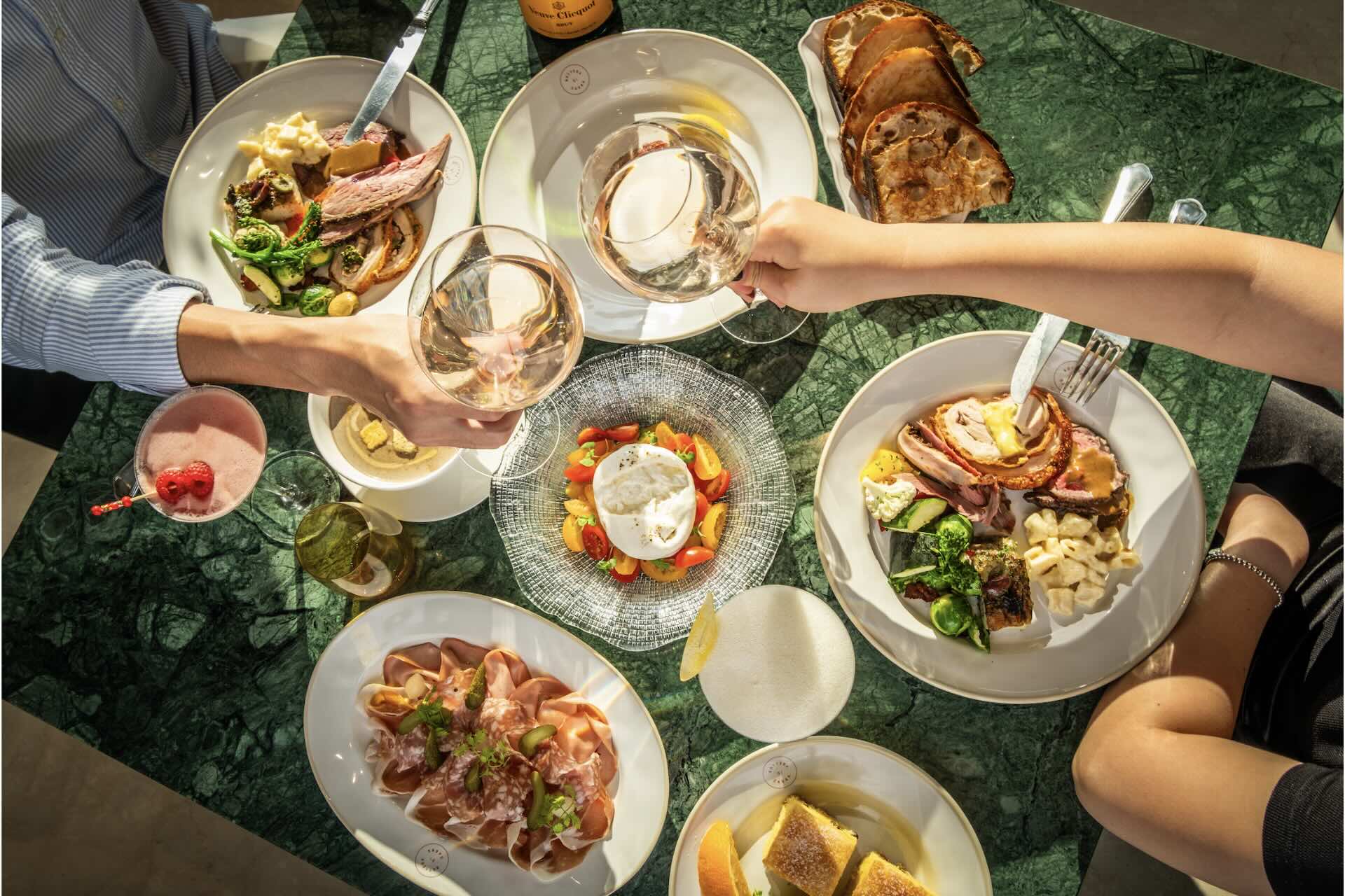 an array of plated food on a green table with hands reaching with forks