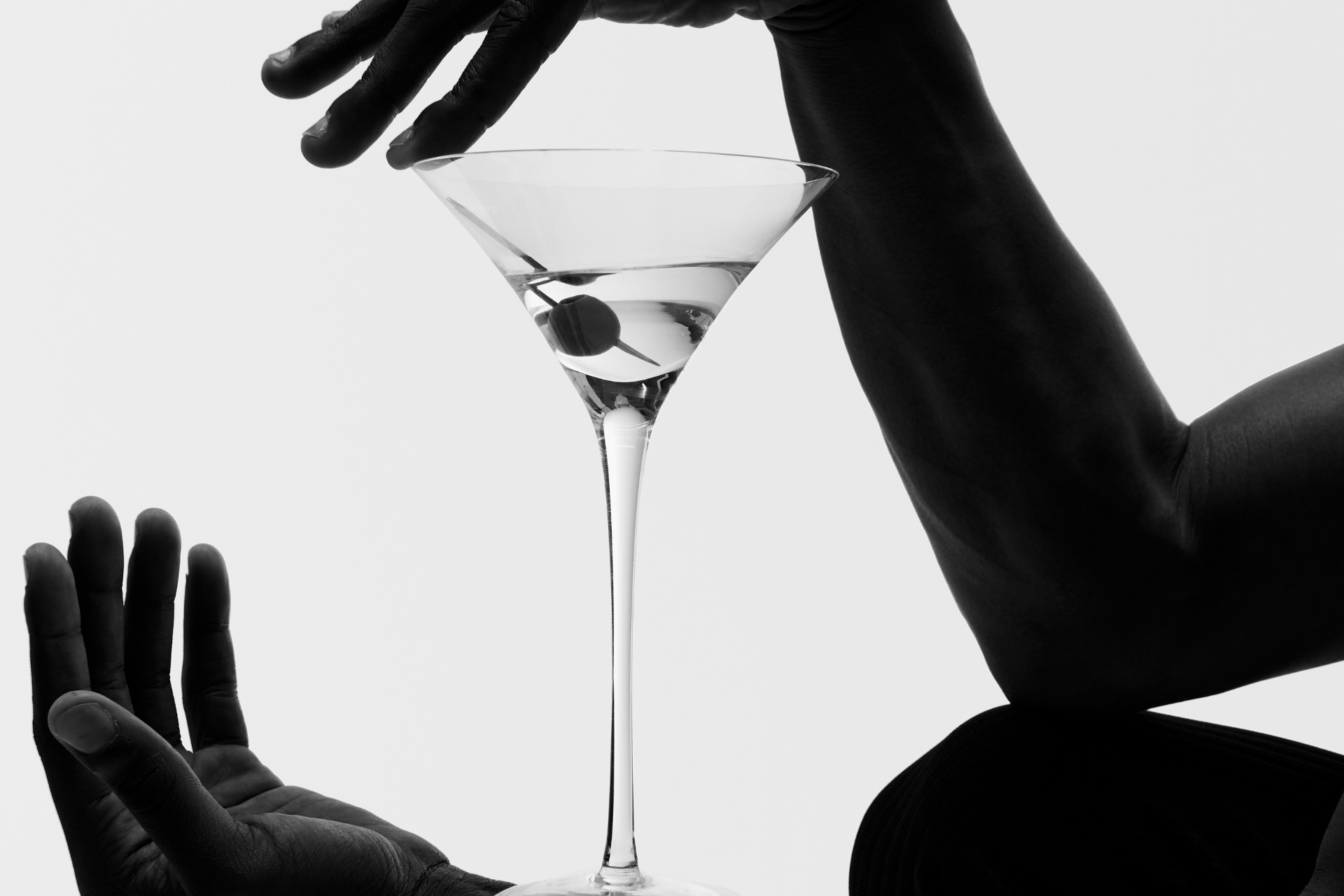 the silhouette of two hands holding a martini with an olive