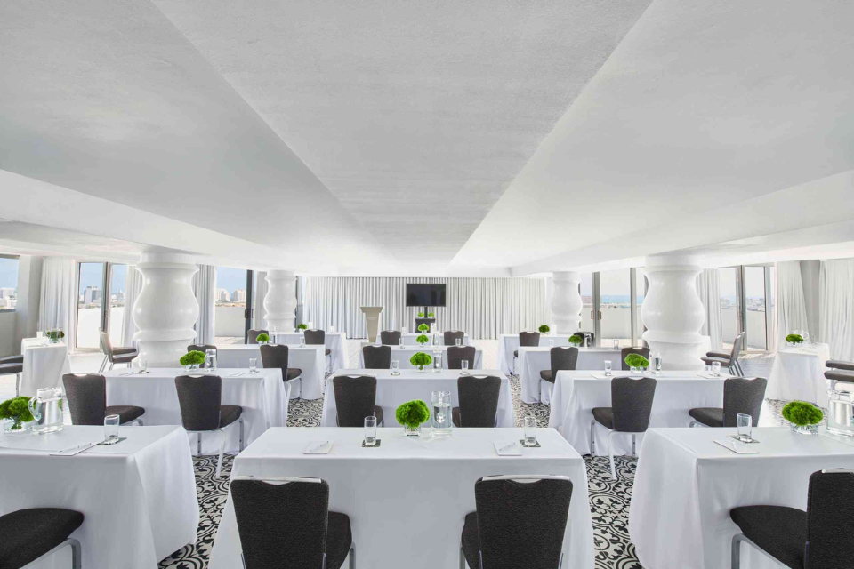 a meeting space set up in classroom style with white linens on each table and black chairs