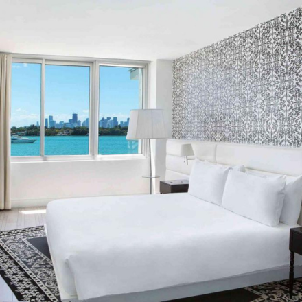 a room with a king bed, dark carpet, wallpaper and views of the bay